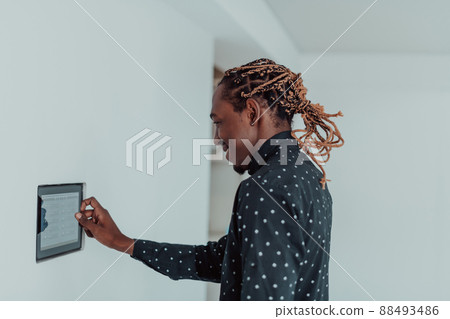 Smiling African American man using modern smart home system, controller on wall, positive young man switching temperature on thermostat or activating security alarm in apartment Smiling African American man using modern smart home system, controller on wall, positive young man switching temperature on thermostat or activating security alarm in apartment 88493486