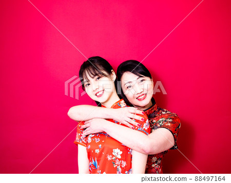 Portrait of a daughter and mother wearing traditional cheongsam qipao and smiling cuddling isolated on red background. Portrait of a daughter and mother wearing traditional cheongsam qipao and smiling cuddling isolated on red background. 88497164