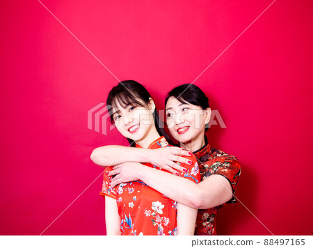 Portrait of a daughter and mother wearing traditional cheongsam qipao and smiling cuddling isolated on red background. 88497165