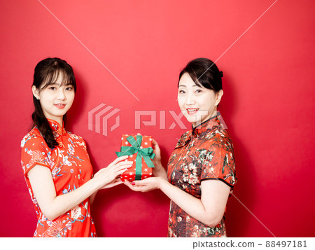 Daughter wearing traditional cheongsam qipao is congratulating mom and giving present wrapped in gift box. Family holiday and togetherness. 88497181