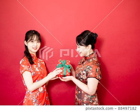 Daughter wearing traditional cheongsam qipao is congratulating mom and giving present wrapped in gift box. Family holiday and togetherness. 88497182