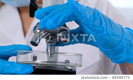 Hands of a researcher laboratory assistant in protective gloves holding a microscope in the 88499773