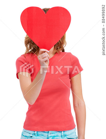 All she can think about is love. A young woman holding a heart-shaped placard over her face while isolated on white. 88499892