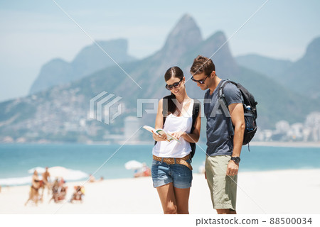 Getting our bearings in paradise. Shot of a young couple looking at a map while standing on a beach. Getting our bearings in paradise. Shot of a young couple looking at a map while standing on a beach. 88500034