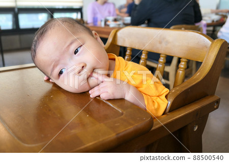 baby sitting in baby chair and sucking finger 88500540