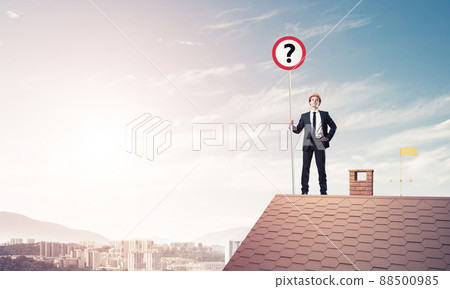 Businessman on brick house roof showing banner with question mar 88500985