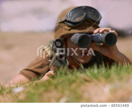 The enemy is in sight. A young soldier looking through his binoculars. 88501489
