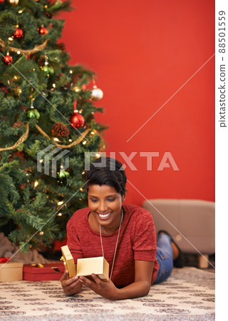 I wonder what it could be. Shot of an attractive young woman opening her gift by the Christmas tree. I wonder what it could be. Shot of an attractive young woman opening her gift by the Christmas tree. 88501559