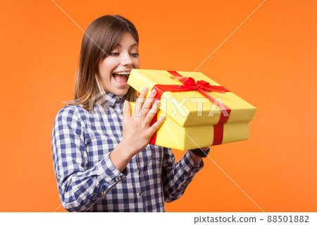 Portrait of shocked charming young woman with brown hair in casual checkered shirt looking into unpacked gift box, curious about birthday surprise. indoor studio shot isolated on orange background Portrait of shocked charming young woman with brown hair in casual checkered shirt looking into unpacked gift box, curious about birthday surprise. indoor studio shot isolated on orange background 88501882