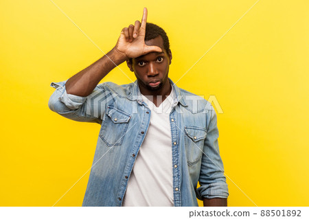 I am loser. Portrait of upset unlucky man in denim casual shirt standing with grumpy face and making loser gesture, unemployed or fired from job. indoor studio shot isolated on yellow background I am loser. Portrait of upset unlucky man in denim casual shirt standing with grumpy face and making loser gesture, unemployed or fired from job. indoor studio shot isolated on yellow background 88501892