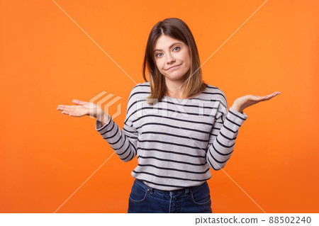 Don't know. Portrait of uncertain confused brunette woman in long sleeve shirt standing having doubts while raised hands, clueless facial expression. indoor studio shot isolated on orange background 88502240