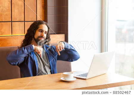 Here and right now. Portrait of angry handsome young leader man freelancer in casual style sitting in cafe and talking in laptop, showing fingers down means here and now. Indoor, lifestyle concept Here and right now. Portrait of angry handsome young leader man freelancer in casual style sitting in cafe and talking in laptop, showing fingers down means here and now. Indoor, lifestyle concept 88502467