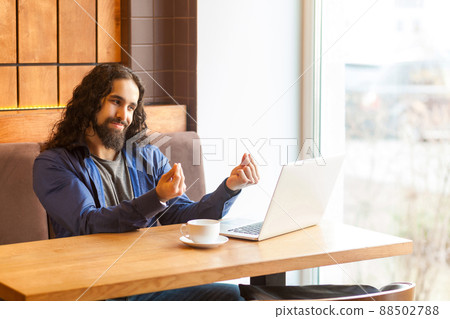 Portrait of handsome young adult man freelancer in casual style sitting in cafe and agrees with his employer for payment through webcam and showing cash gesture with smile. Indoor, lifestyle concept Portrait of handsome young adult man freelancer in casual style sitting in cafe and agrees with his employer for payment through webcam and showing cash gesture with smile. Indoor, lifestyle concept 88502788