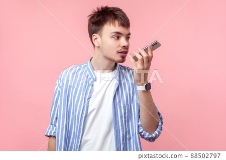 Voice application. Portrait of brown-haired man with small beard and mustache in casual striped shirt talking on phone, using digital vocal assistant for command recorder or calling. isolated on pink 88502797