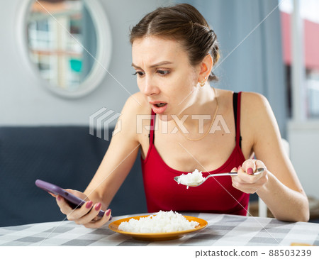 Frustrated woman using smartphone while eating rice 88503239
