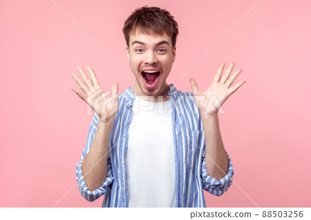 Unbelievable news. Portrait of shocked brown-haired man with big eyes and open mouth raising hand, looking at camera with stunned astonished face. indoor studio shot isolated on pink background Unbelievable news. Portrait of shocked brown-haired man with big eyes and open mouth raising hand, looking at camera with stunned astonished face. indoor studio shot isolated on pink background 88503256