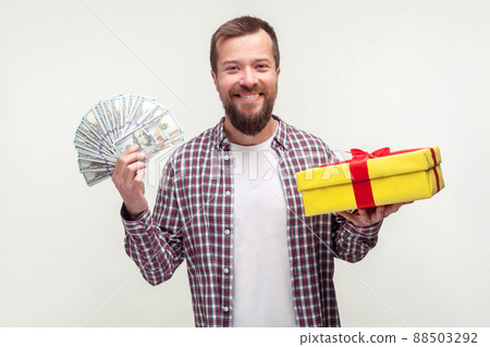 Cashback and present for buyer. Portrait of happy bearded man in casual plaid shirt holding wrapped box and dollars, smiling satisfied with gift. indoor studio shot isolated on white background Cashback and present for buyer. Portrait of happy bearded man in casual plaid shirt holding wrapped box and dollars, smiling satisfied with gift. indoor studio shot isolated on white background 88503292