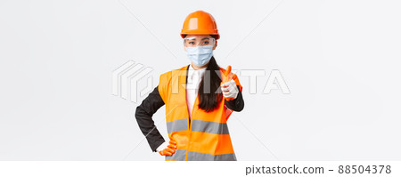 Covid-19 safety protocol at enterpise, construction and preventing virus concept. Confident asian female engineer, architect in face mask and helmet showing thumb-up, guarantee quality of building 88504378