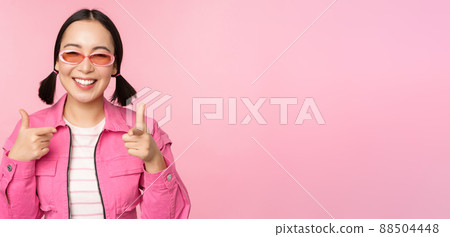 Close up portrait of modern asian girl in sunglasses smiling, pointing fingers at camera, praise you, inviting or complimenting, standing over pink background Close up portrait of modern asian girl in sunglasses smiling, pointing fingers at camera, praise you, inviting or complimenting, standing over pink background 88504448