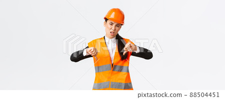 Disappointed and upset asian female chief engineer inspect bad work, showing thumbs-down disappointed, wear safety helmet and complaining weak awful work of architect, white background Disappointed and upset asian female chief engineer inspect bad work, showing thumbs-down disappointed, wear safety helmet and complaining weak awful work of architect, white background 88504451