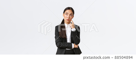 Thoughtful serious-looking asian female manager, office worker in suit thinking about solution, making hard choice, looking away while pondering, standing white background Thoughtful serious-looking asian female manager, office worker in suit thinking about solution, making hard choice, looking away while pondering, standing white background 88504894