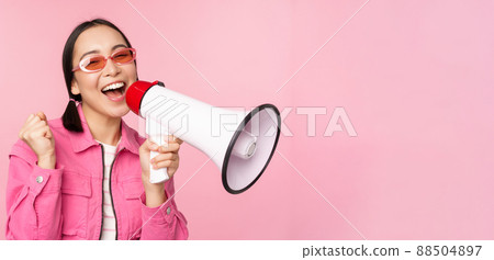 Attention, announcement concept. Enthusiastic asian girl shouting in megaphone, advertising with speaker, recruiting, standing over pink background Attention, announcement concept. Enthusiastic asian girl shouting in megaphone, advertising with speaker, recruiting, standing over pink background 88504897