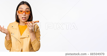 Image of happy asian girl talking on speakerphone, recording, translating her voice with mobile phone app, talking in smartphone dynamic, standing over white background Image of happy asian girl talking on speakerphone, recording, translating her voice with mobile phone app, talking in smartphone dynamic, standing over white background 88504970