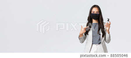 Business, finance and employment, covid-19 preventing virus and social distancing concept. Smiling cute asian office worker in face mask recommend using hand sanitizer while at work Business, finance and employment, covid-19 preventing virus and social distancing concept. Smiling cute asian office worker in face mask recommend using hand sanitizer while at work 88505046