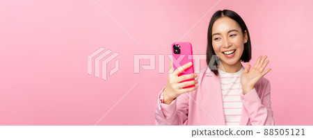 Stylish asian businesswoman, girl in suit taking selfie on smartphone, video chat with mobile phone app, posing against pink studio background 88505121