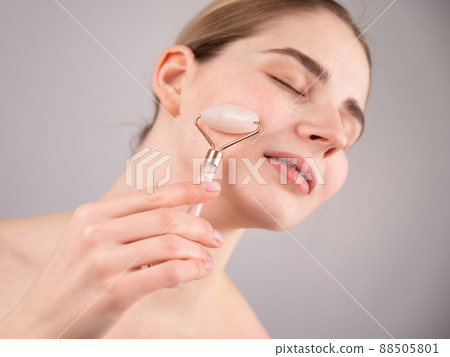 Close-up portrait of a woman using a quartz roller massager on her cheek for an alternative anti-aging. 88505801