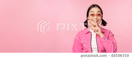 Modern korean girl in stylish spring outfit, sunglasses, showing shush, hush sign, press finger to lips, taboo gesture, standing over pink background Modern korean girl in stylish spring outfit, sunglasses, showing shush, hush sign, press finger to lips, taboo gesture, standing over pink background 88506359