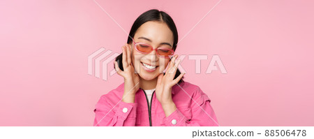 Close up of stylish korean girl in sunglasses, smiling happy, posing against pink background. People face concept 88506478