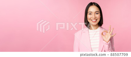 Excellent work, well done gesture. Smiling asian businesswoman showing okay, ok sign, praise good work, recommending company, looking as confident professional, pink background 88507709
