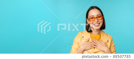 Close up portrait of asian young woman in sunglasses, smiling and looking romantic, standing happy over blue background 88507785