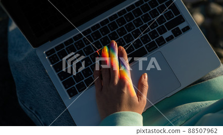 A woman is typing on a laptop. Rainbow light from a prism.  88507962