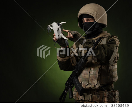 a soldier in military clothes with a weapon launches a small unmanned quadcopter for reconnaissance on a dark background a soldier in military clothes with a weapon launches a small unmanned quadcopter for reconnaissance on a dark background 88508489