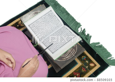 Muslim woman in a veil sitting on the prayer rug and reading the Quran 88509103