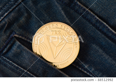 A golden physical TRON coin sticks out of the pocket of blue jeans close-up. A golden physical TRON coin sticks out of the pocket of blue jeans close-up. 88512992