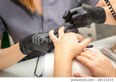 Manicure master in rubber gloves applies an electric nail file to remove the nail polish in a nail salon Manicure master in rubber gloves applies an electric nail file to remove the nail polish in a nail salon 88513254