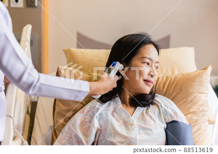 Nurse checking patient's temperature in the ear with Tympanic Thermometer in hospital ward. 88513619