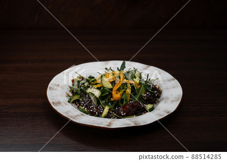 Chicken liver salad with fresh cucumber slices with bell pepper with arugula in honey sauce with sesame on a wooden table in a restaurant. National Georgian dish. 88514285