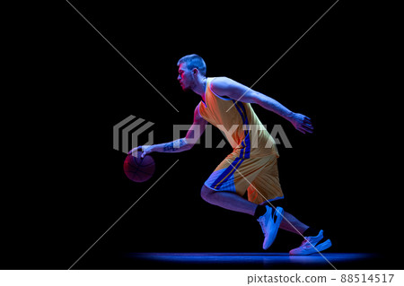 Dribbling. One sportive man, professional basketball player playing basketball isolated on dark background in neon light. Achievements, sport career, motion concepts. 88514517