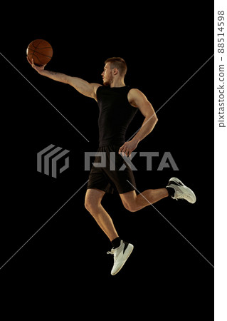 Dynamic portrait of young man, basketball player in black uniform training isolated on dark background. Achievements, sport career, motion concepts.