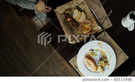 Woman is sitting at a wooden dining wooden table in a restaurant with fish tartare and baked fish fillet with vegetables. Lunch break. Great seafood snacks Woman is sitting at a wooden dining wooden table in a restaurant with fish tartare and baked fish fillet with vegetables. Lunch break. Great seafood snacks 88515986