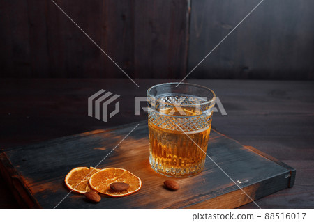 Amazing golden Scotch whiskey in a crystal glass decorated with sweet orange slices and peanuts, stands on an old wooden table in a pub. Delicious male drink. Weekend at the bar 88516017