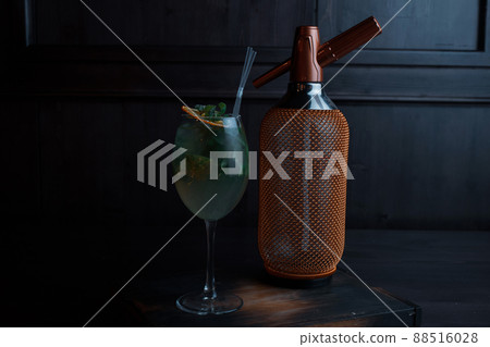 Amazing alcoholic cocktail in an elegant glass with tequila with vanilla syrup and fresh mint leaves stands on a vintage table in a bar near a golden luxury bottle. Drink with orange slices. Close-up 88516028