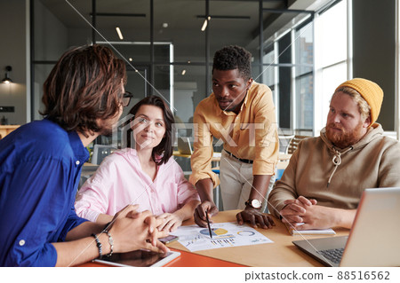 Group of young interracial colleagues viewing report and discussing analytical data at meeting in office Group of young interracial colleagues viewing report and discussing analytical data at meeting in office 88516562