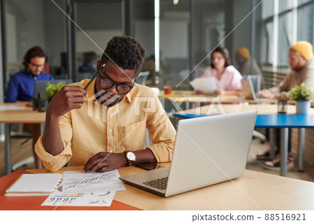 Thoughtful Black strategy manager sitting in coworking space and examining documents 88516921