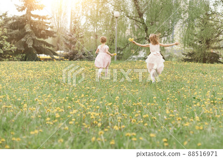 two little sisters running across the lawn on a spring day . 88516971