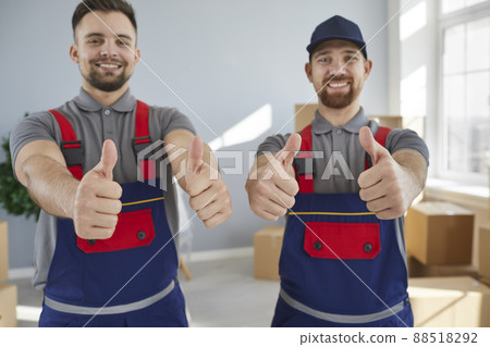 Two smiling young male employees of moving and cargo delivery company show thumbs up. Two smiling young male employees of moving and cargo delivery company show thumbs up. 88518292